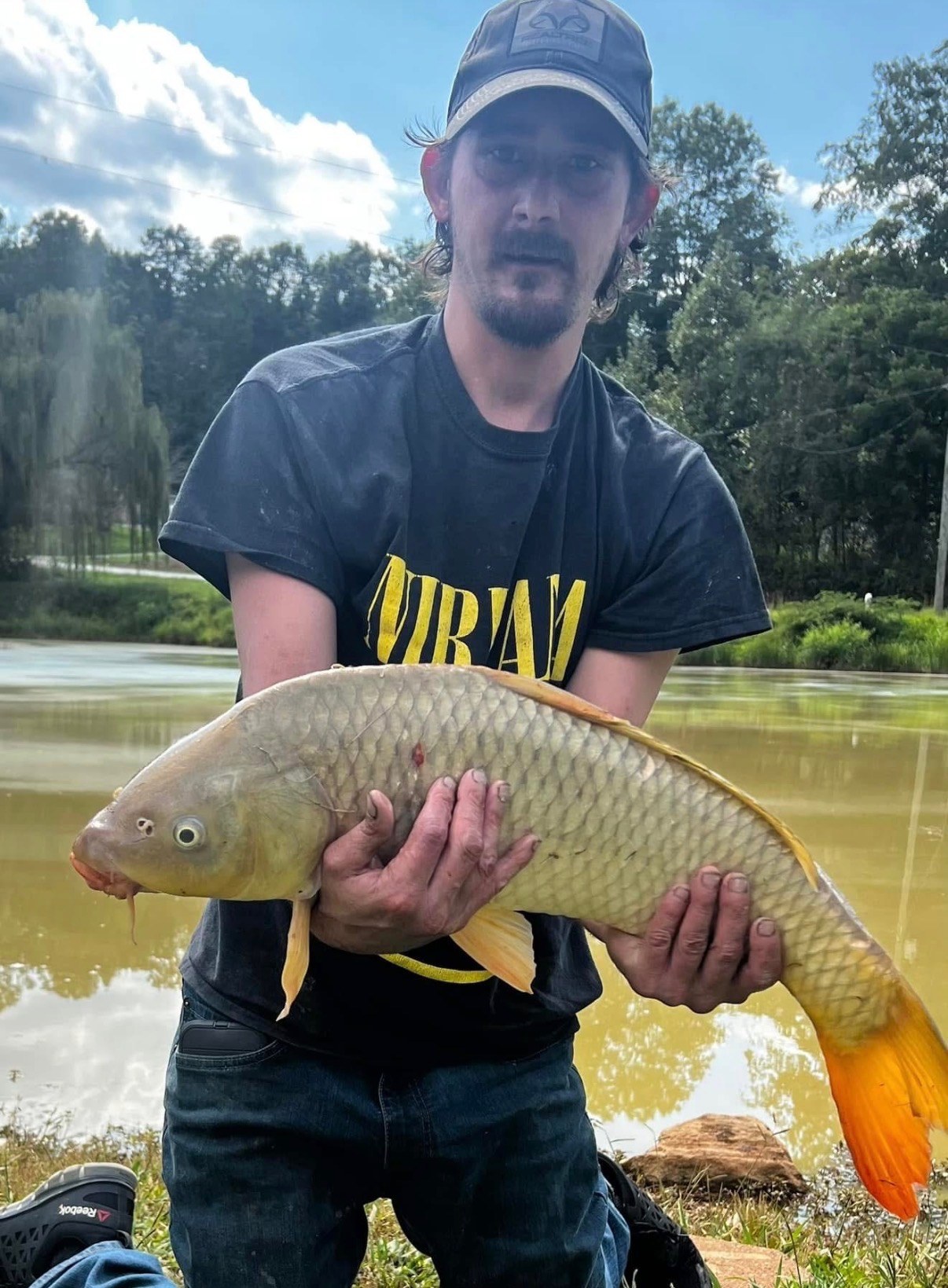Angler holding a golden carp beside a pond