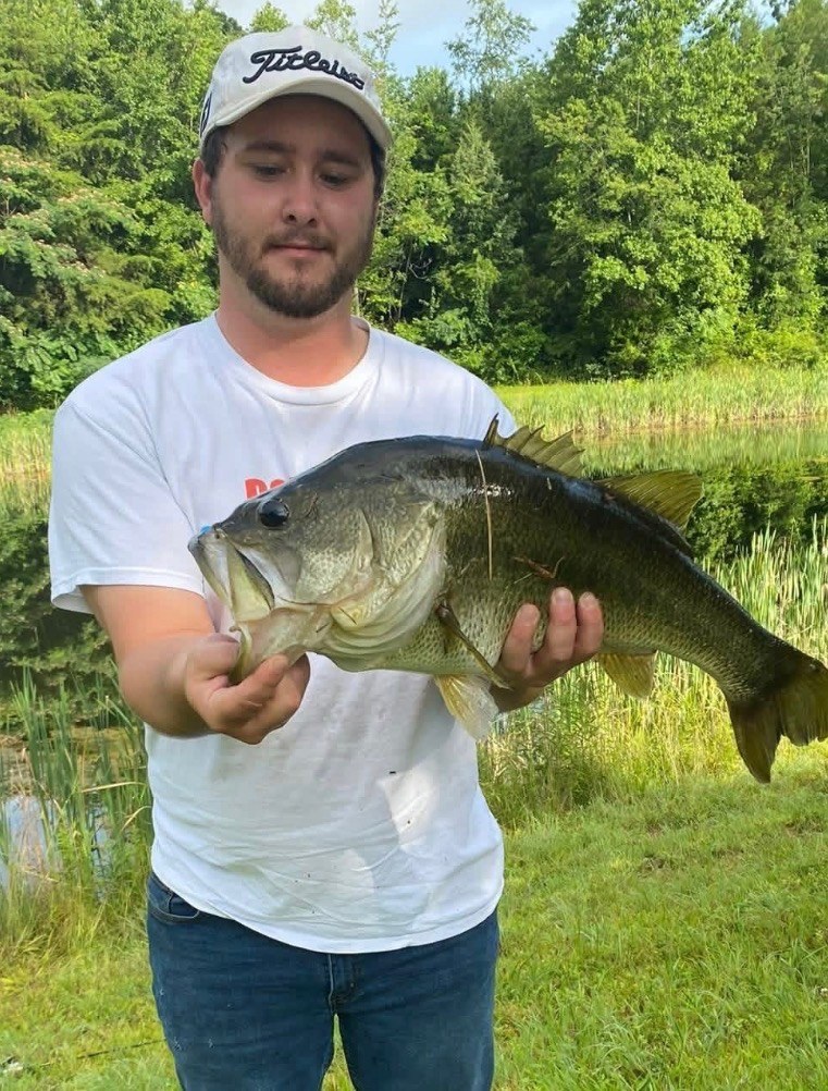 Angler holding a largemouth bass in front of a green pond