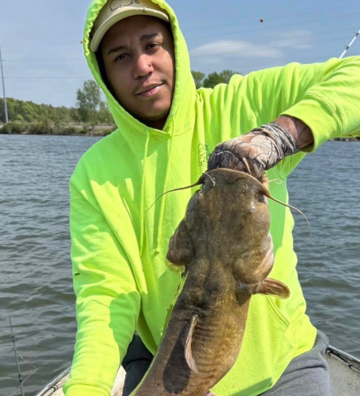 Angler in a neon hoodie holding a catfish from a boat
