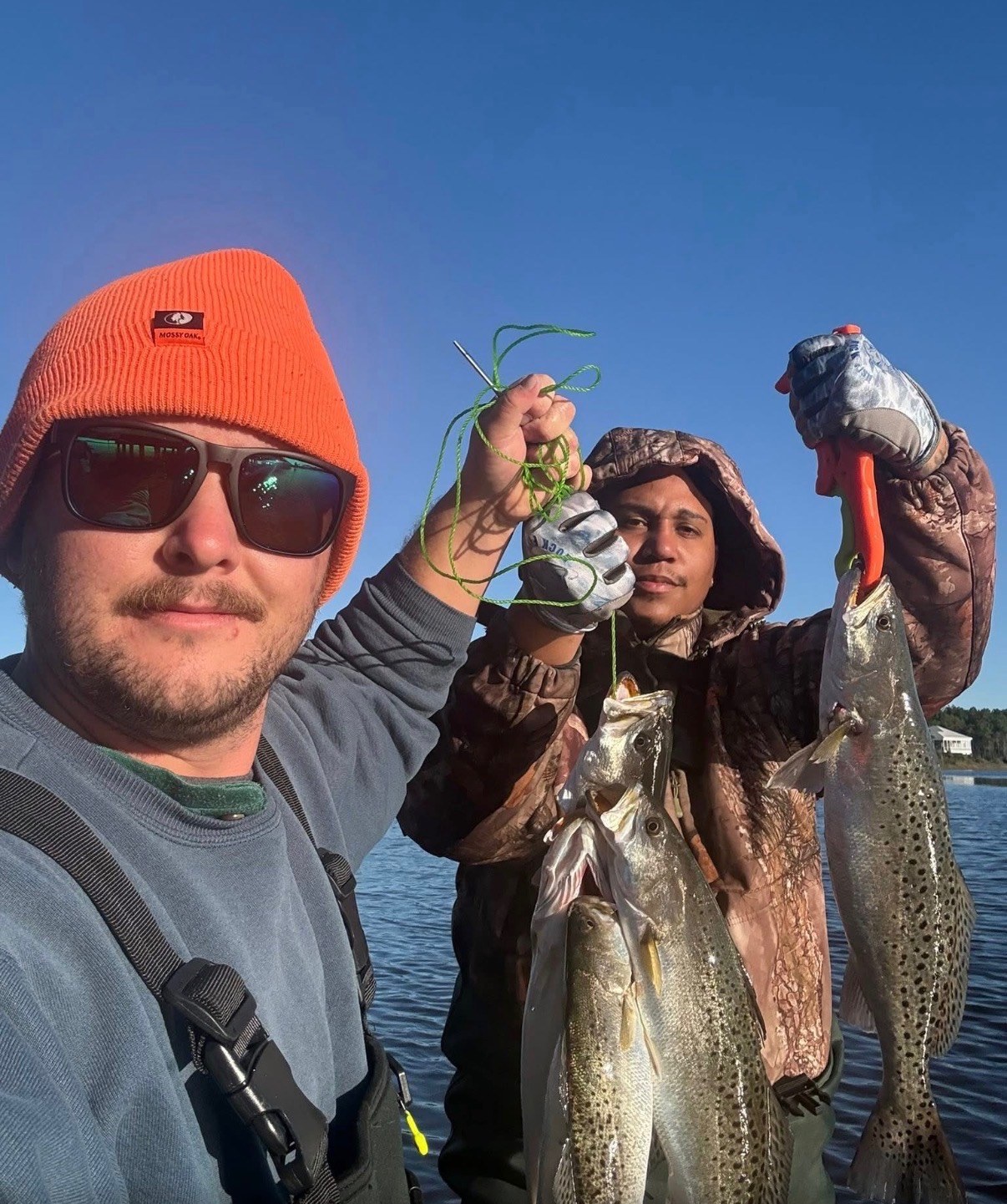 Two anglers holding a stringer of speckled trout on the water